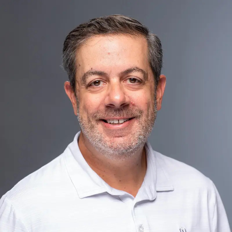 A man with grey hair and beard wearing white shirt.